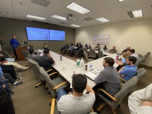 Man in blue shirt giving a speech to a group of people in a conference room